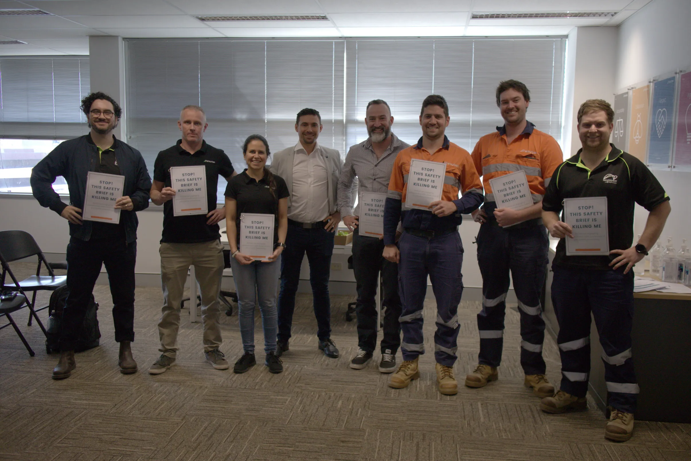 Workshop participants holding signs reading 'STOP! This safety brief is killing me'